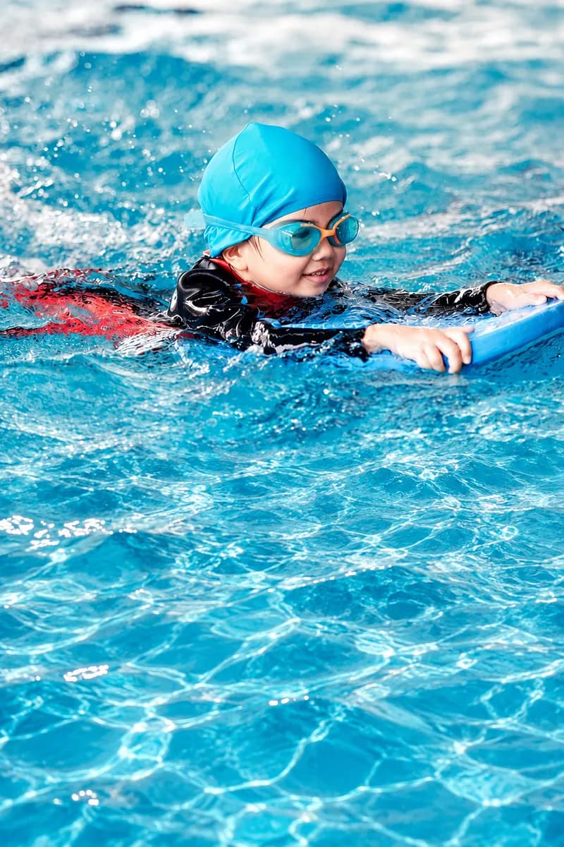 Enfant avec bonnet et lunettes nageant avec une planche